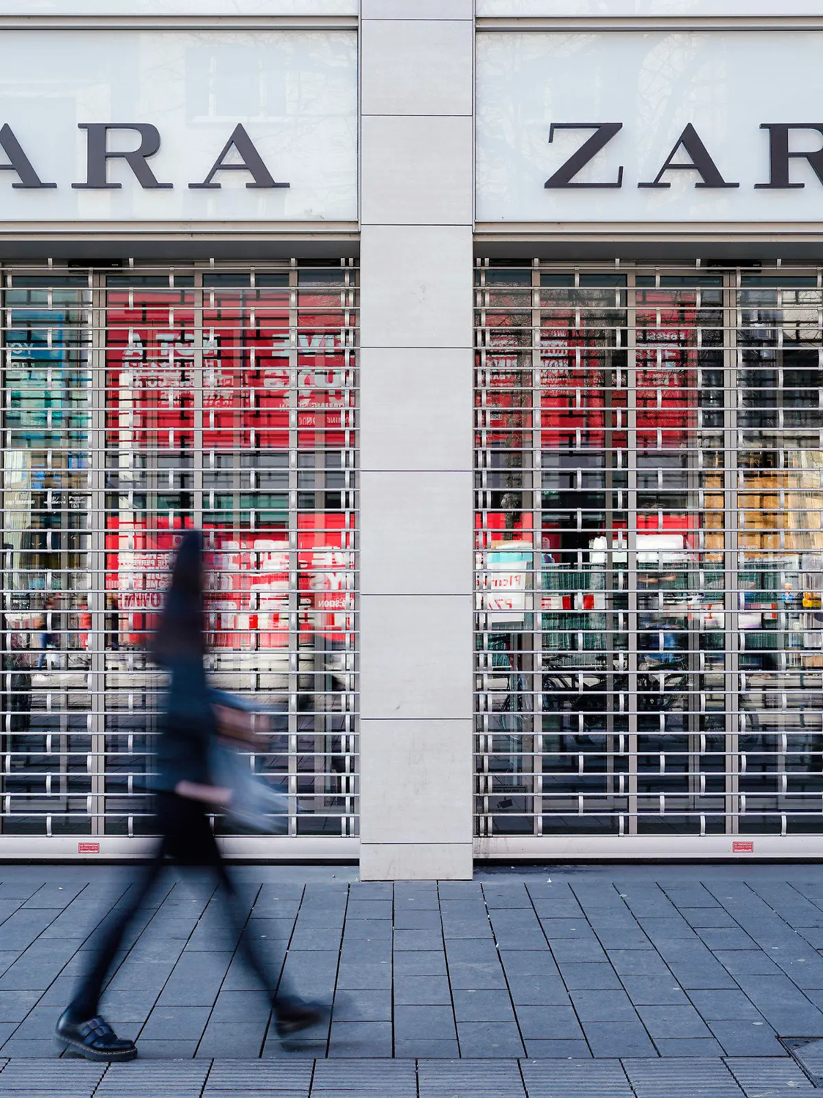 ARCHIV - 18.03.2020, Baden-Württemberg, Mannheim: Eine Fußgängerin geht vormittags in der Einkaufsstraße Planken an einem mit Gitter verschlossenen Eingang eines Zara-Bekleidungsgeschäfts vorbei. Der spanische Textilhändler Inditex ist wegen der Corona-Pandemie erstmals seit vielen Jahren in die roten Zahlen gerutscht. (zu dpa "Corona-Krise brockt Zara-Mutterkonzern Inditex Quartalsverlust ein") Foto: Uwe Anspach/dpa +++ dpa-Bildfunk +++