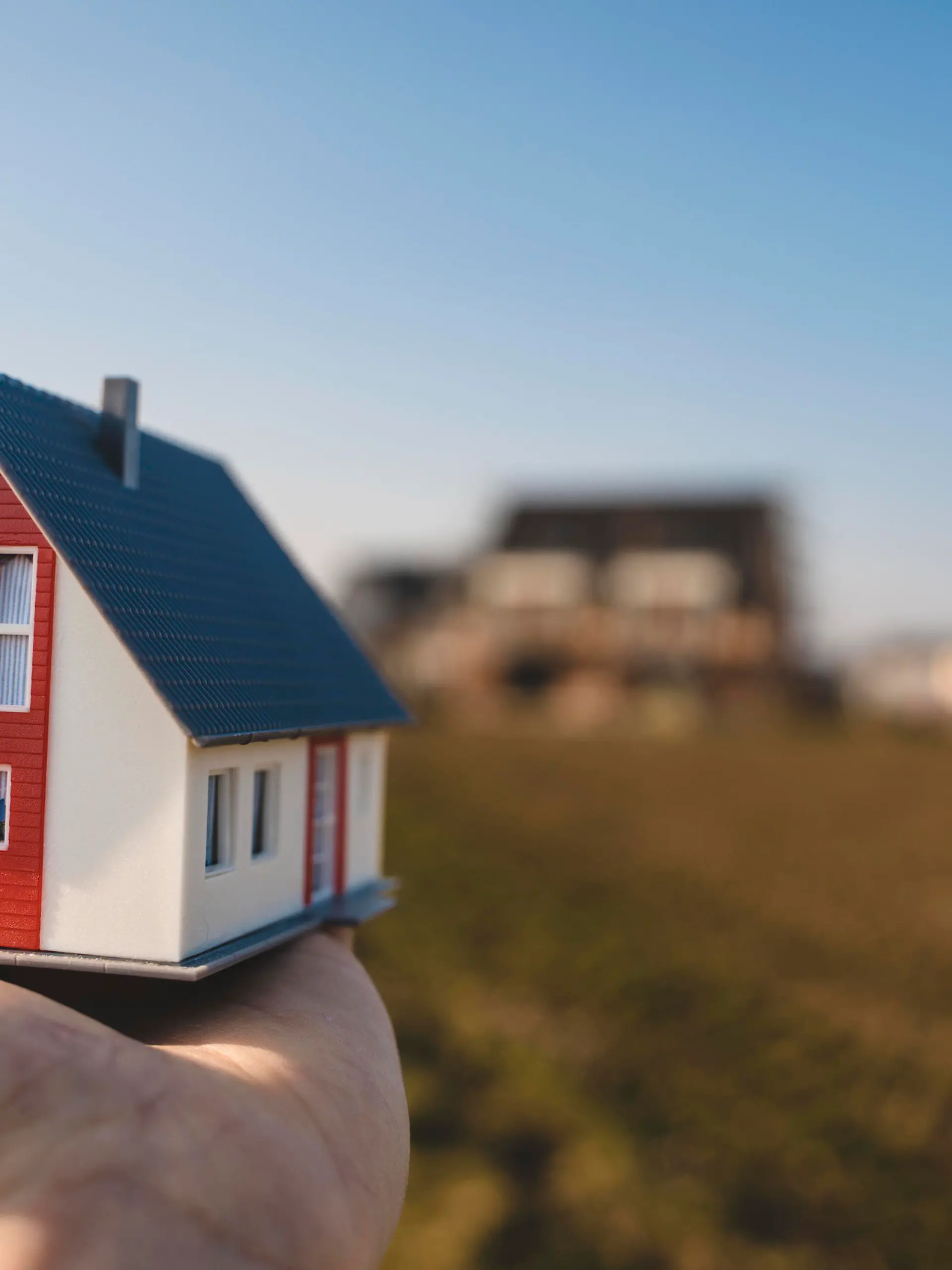 Traum vom Eigenheim, Hand hält ein Modelhaus über ein Baugrundstück, Traumhaus Konzept