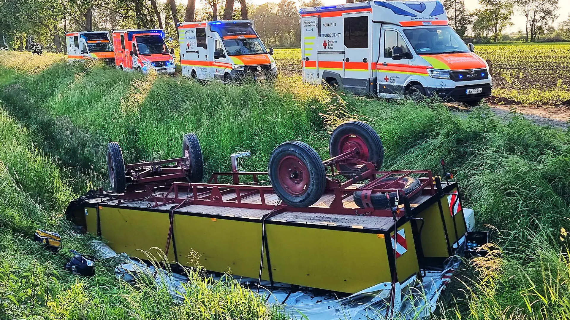 28.05.2023, Niedersachsen, Andervenne: Krankenwagen stehen an der Unfallstelle, an der im Emsland ein mit Ausflüglern besetzter Planwagen in einen Graben gestürzt war. Bei dem Unfall mit dem Planwagen sind zwei Frauen im Alter von 19 und 53 Jahren sowie ein 58-jähriger Mann bei Andervenne (Landkreis Emsland) schwer verletzt worden. Neun weitere Mitfahrende zwischen 18 und 82 Jahren kamen mit leichten Verletzungen davon, wie die Polizei mitteilte. Die Gruppe saß am Sonntagabend während eines Familienausflugs in dem Planwagen, der von einem Traktor gezogen wurde, als die Verbindung zwischen beiden Fahrzeugen riss. Der Planwagen rutschte vom Schotterweg in einen Graben und kam dort auf dem Dach zum Liegen. Grund für den Unfall war vermutlich eine gerissene Schweißnaht. Die Verletzten kamen in ein Krankenhaus. Foto: -/NWM-TV/dpa +++ dpa-Bildfunk +++