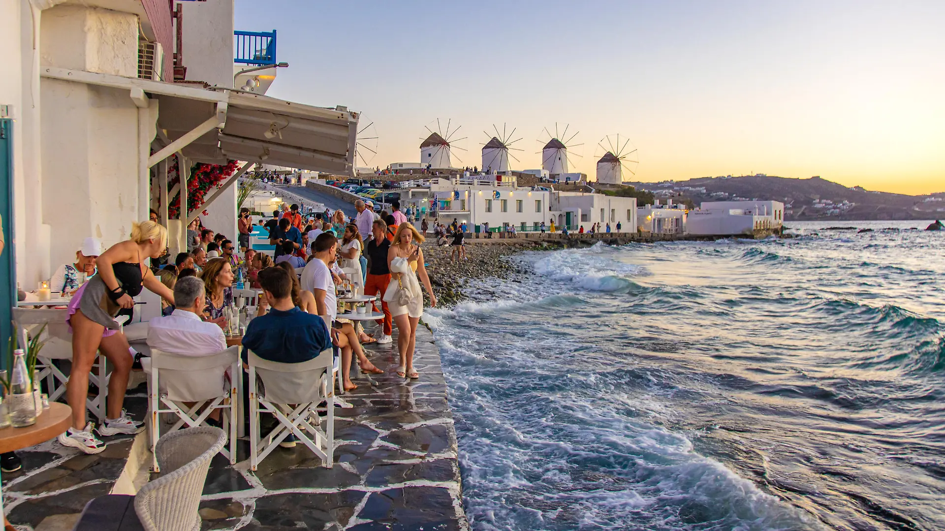 The iconic windmills of Mykonos island as seen from Little Venice with tourists at the bars, cafes and restaurants. Mykonos is an island in Greece in the Aegean sea. There are 16 windmills on the island, 5 of them above Chora, the main town in the island. The windmills were built in the 16th century from the Venetians but their constructions continued until the 20th century. Sunset with people at the windmills in Mykonos. Tourists enjoy a beautiful sunset during the magic hour at Mykonos island in Greece. The Greek island of Myconos is a popular glamorous Mediterranean travel destination for holidays in the Cyclades, Aegean Sea with the iconic whitewashed buildings, the sandy beaches and famous party at the beach bars. The tourism and travel industry had a negative impact in the business and local economy sector due to the Covid-19 Coronavirus pandemic. Mykonos island, Greece(Photo by Nicolas Economou/NurPhoto)