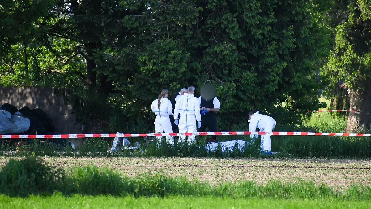 27.05.2023, Bayern, Sauerlach: Mitarbeiter der Spurensicherung und Bestatter stehen am Fundort einer Frauenleiche. Eine junge Frau ist am Samstag in Sauerlach bei München tot auf einem Feldweg gefunden worden. Die Polizei geht von einem Tötungsdelikt aus. Ein Mann, der selbst schwer verletzt sei, sei tatverdächtig, sagte ein Polizeisprecher. Foto: Vifogra/Tiedemann/vifogra/dpa - ACHTUNG: Person(en) wurde(n) aus rechtlichen Gründen gepixelt +++ dpa-Bildfunk +++