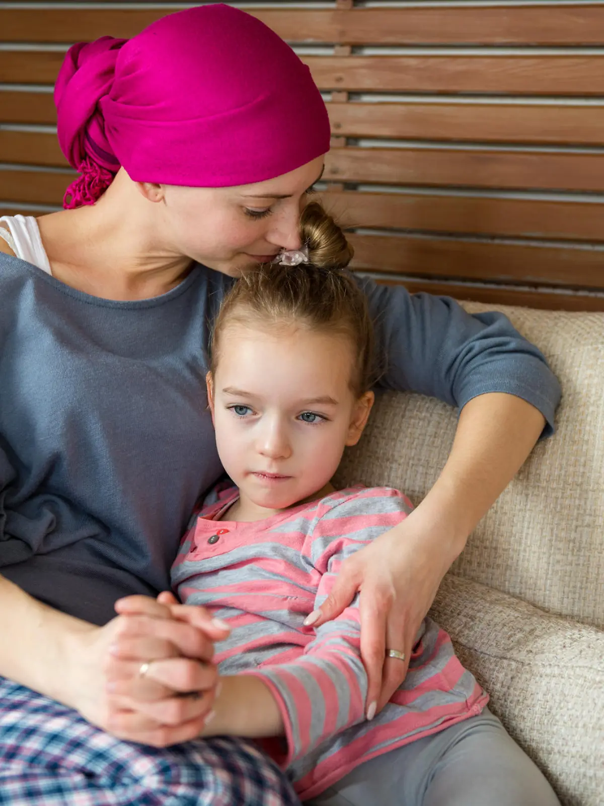Young adult female cancer patient spending time with her daughter at home, relaxing on the couch. Cancer and family support concept.