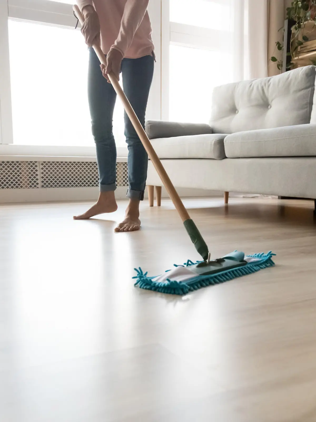 Cropped close up image of barefoot young woman in casual clothes washing heated wooden laminate warm floor using microfiber wet mop pad, doing homework cleaning routine, housekeeping job concept