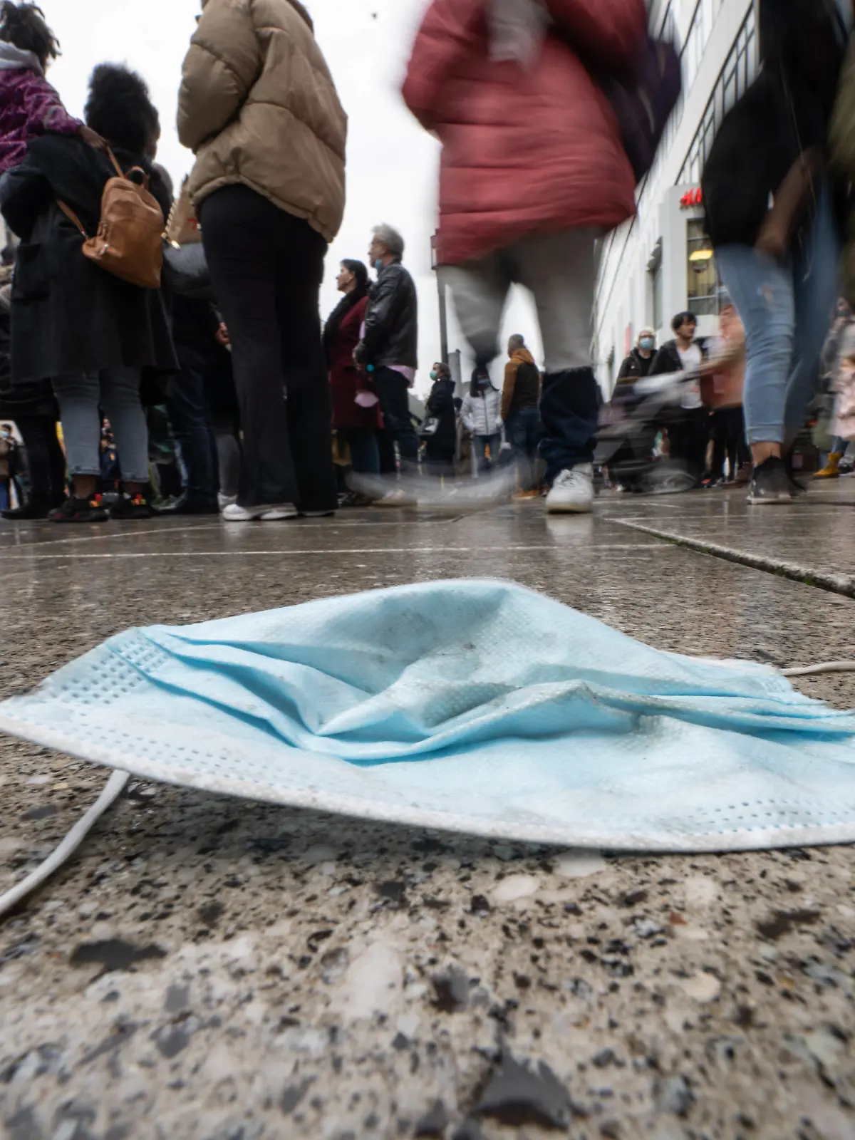 30.10.2021, Hessen, Frankfurt/Main: Ein verlorener Mund-Nasen-Schutz liegt am Nachmittag auf dem nassen Pflaster von Frankfurts zentraler Einkaufsmeile, der Zeil. Die Sieben-Tage-Inzidenz der Corona-Infektionen in Hessen ist am gleichen Tag (30.10.2021) weiter gestiegen. (Aufnahme mit längerer belichtungszeit und absichtlicher Bewegung der Kamera) Foto: Frank Rumpenhorst/dpa +++ dpa-Bildfunk +++