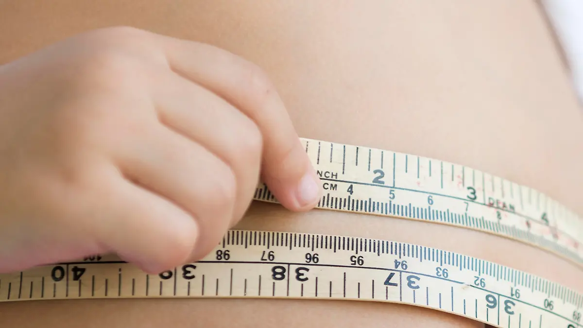 cute girl measuring her belly with measurement tape at home