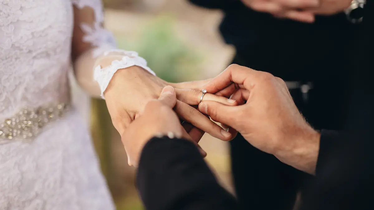 Closeup of groom placing a wedding ring on the brides hand.  Couple exchanging wedding rings during a wedding ceremony outdoors.