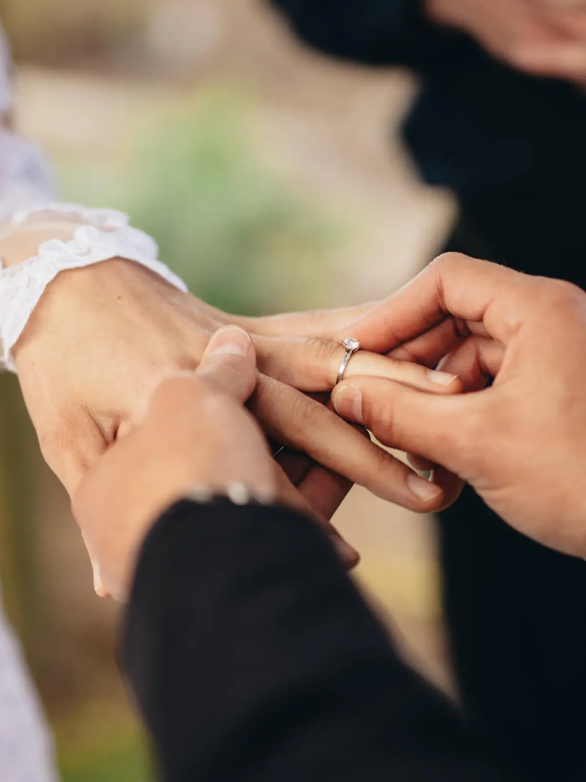 Closeup of groom placing a wedding ring on the brides hand.  Couple exchanging wedding rings during a wedding ceremony outdoors.