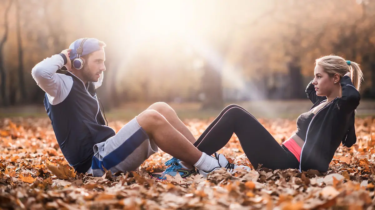 Young athletes exercising sit-ups together in the park and looking at each other.
