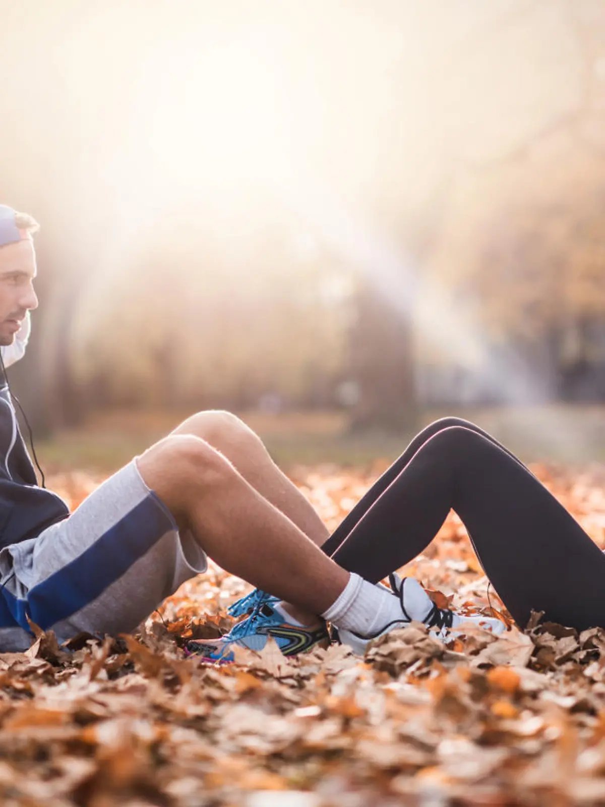 Young athletes exercising sit-ups together in the park and looking at each other.