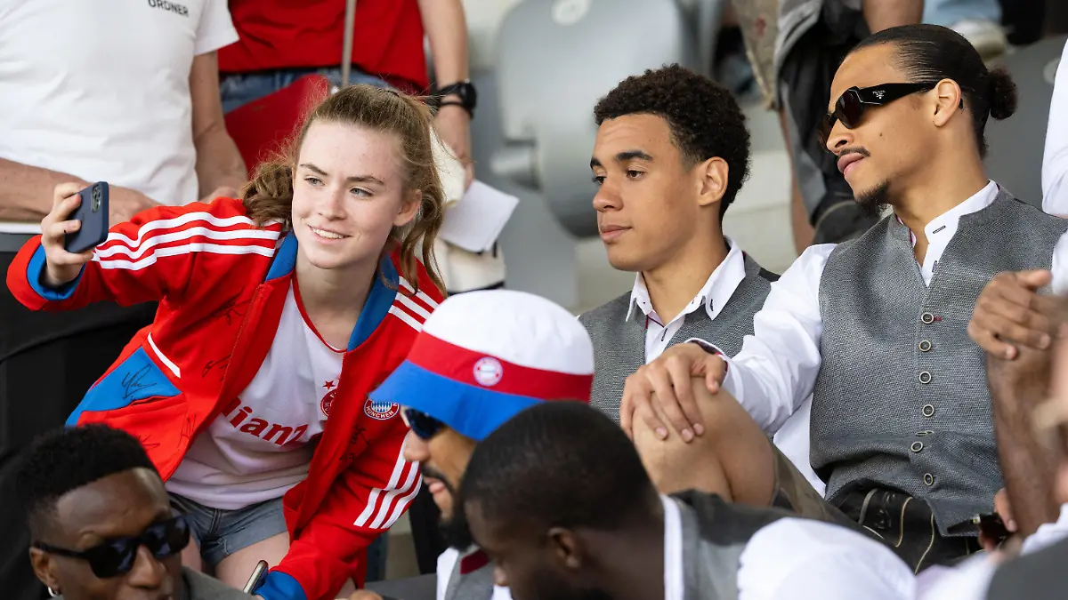 28.05.2023, Bayern, München: Fußball, Frauen: Bundesliga, Bayern München - Turbine Potsdam, 22. Spieltag am FC Bayern Campus. Jamal Musiala (M) und Leroy Sane (r) von München verfolgen das Spiel auf der Tribüne und machen ein Foto mit einem Fan. Foto: Sven Hoppe/dpa - WICHTIGER HINWEIS: Gemäß den Vorgaben der DFL Deutsche Fußball Liga bzw. des DFB Deutscher Fußball-Bund ist es untersagt, in dem Stadion und/oder vom Spiel angefertigte Fotoaufnahmen in Form von Sequenzbildern und/oder videoähnlichen Fotostrecken zu verwerten bzw. verwerten zu lassen. +++ dpa-Bildfunk +++
