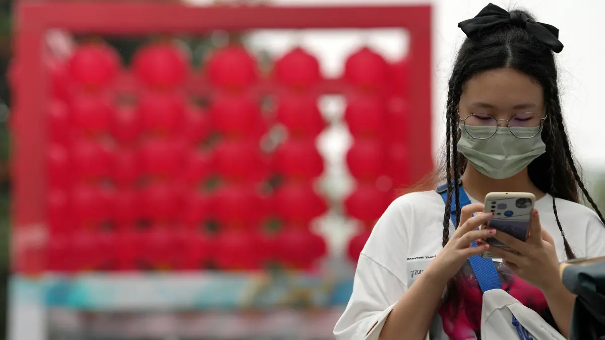 14.08.2022, China, Beijing: Eine Frau, die eine Mund-Nasen-Schutz trägt, überprüft in der Nähe eines Einkaufszentrums ihr Telefon. China hat die höchsten Corona-Infektionszahlen seit über drei Monaten gemeldet. Foto: Ng Han Guan/AP/dpa +++ dpa-Bildfunk +++