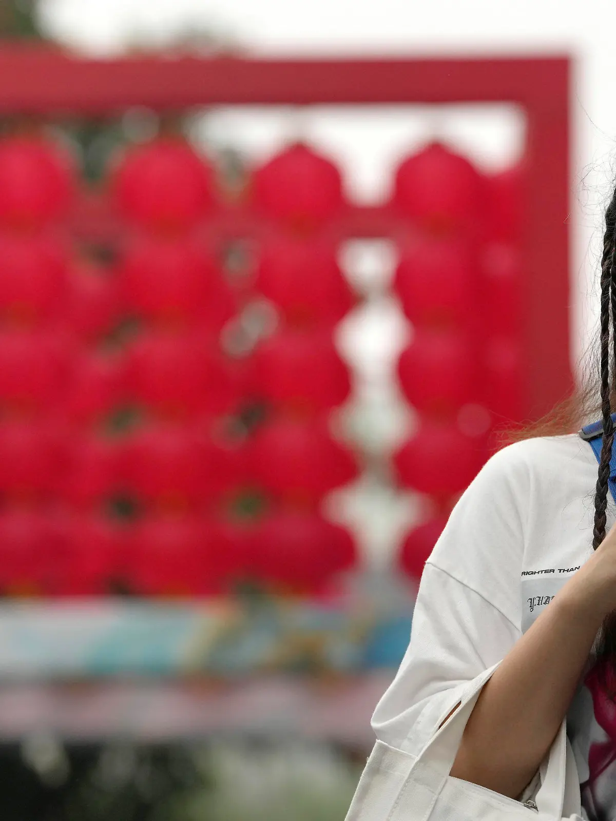 14.08.2022, China, Beijing: Eine Frau, die eine Mund-Nasen-Schutz trägt, überprüft in der Nähe eines Einkaufszentrums ihr Telefon. China hat die höchsten Corona-Infektionszahlen seit über drei Monaten gemeldet. Foto: Ng Han Guan/AP/dpa +++ dpa-Bildfunk +++