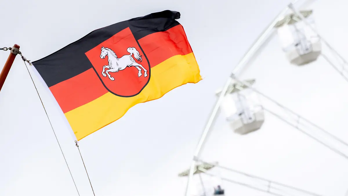 ARCHIV - 22.05.2021, Niedersachsen, Bensersiel: Eine niedersächsische Flagge weht vor einem Riesenrad im Hafen von Bensersiel an der Nordseeküste. Das Bundesland Niedersachsen feiert am 1. November sein 75-jähriges Bestehen. (Zu dpa: «Historiker: Niedersachsen ist erfolgreiche Integrationsgeschichte») Foto: Hauke-Christian Dittrich/dpa +++ dpa-Bildfunk +++