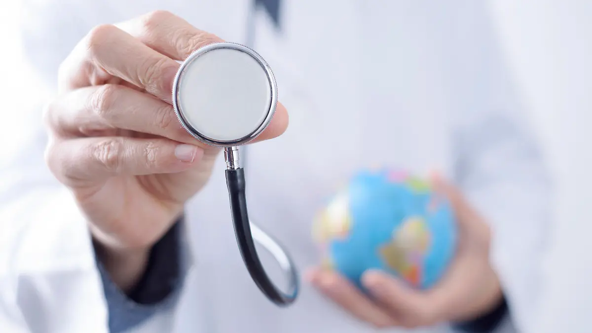 closeup of a young caucasian doctor man with a world globe in one hand and a stethoscope in the other hand