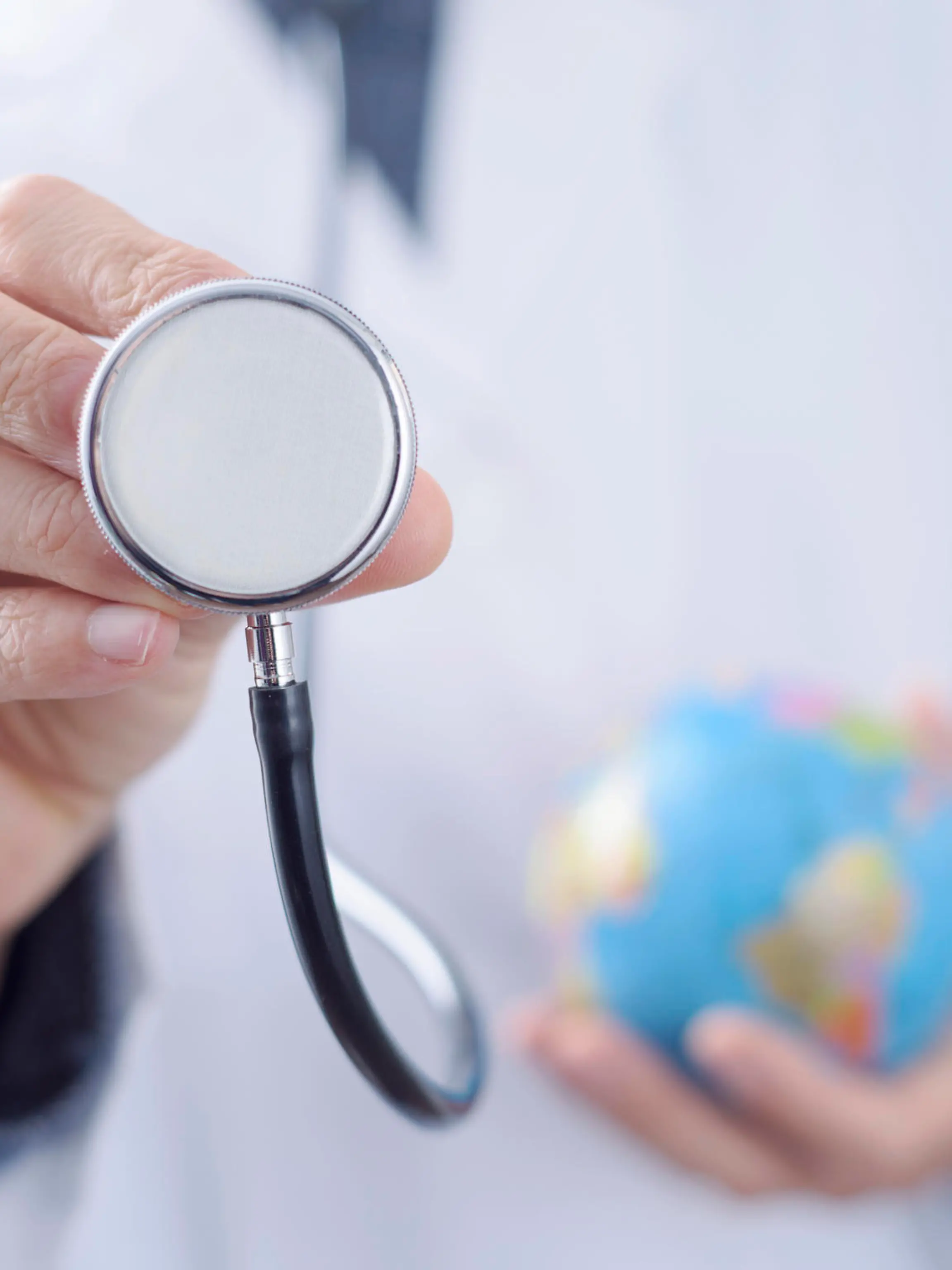 closeup of a young caucasian doctor man with a world globe in one hand and a stethoscope in the other hand
