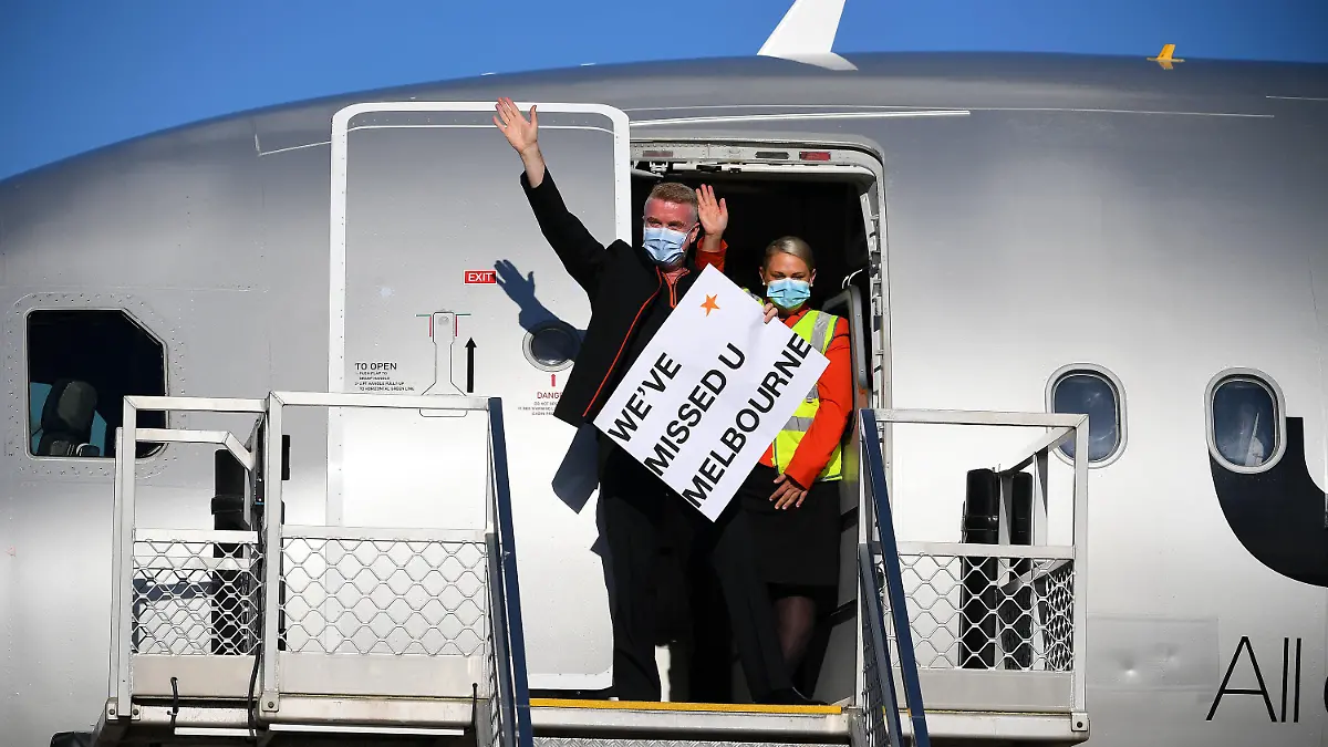 01.11.2021, Australien, Melbourne: Die Flugbesatzung winkt den Medien mit einem Schild im Türrahmen des Jetstar-Flugs JQ505, der am Montag, dem 1. November 2021, auf dem Tullamarine Airport in Melbourne aus Sydney angekommen ist. Die ersten Passagiere, die ohne Quarantänebeschränkungen reisen, sind am Flughafen Melbourne eingetroffen. Foto: James Ross/AAP/dpa +++ dpa-Bildfunk +++