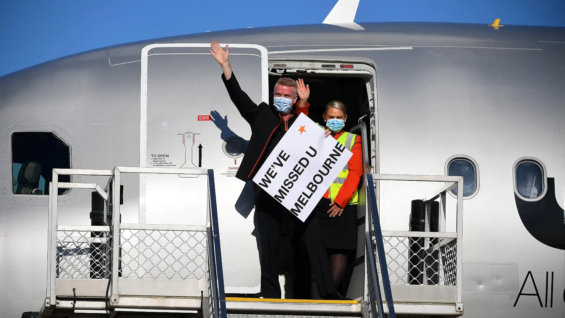 01.11.2021, Australien, Melbourne: Die Flugbesatzung winkt den Medien mit einem Schild im Türrahmen des Jetstar-Flugs JQ505, der am Montag, dem 1. November 2021, auf dem Tullamarine Airport in Melbourne aus Sydney angekommen ist. Die ersten Passagiere, die ohne Quarantänebeschränkungen reisen, sind am Flughafen Melbourne eingetroffen. Foto: James Ross/AAP/dpa +++ dpa-Bildfunk +++