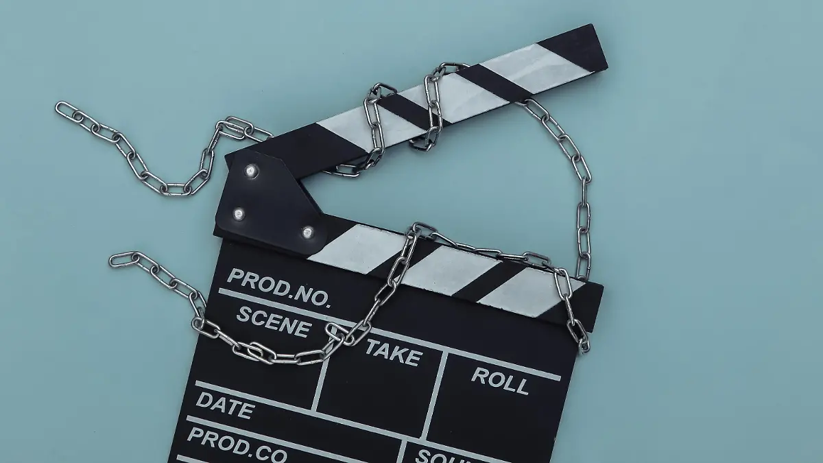 Movie clapperboard wrapped in steel chain on blue background. Ban on filmmaking. Top view