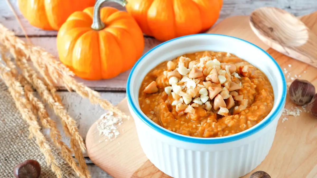                                 Bowl of autumn pumpkin oatmeal with walnuts, chocolate and peanut butter chips, table scene