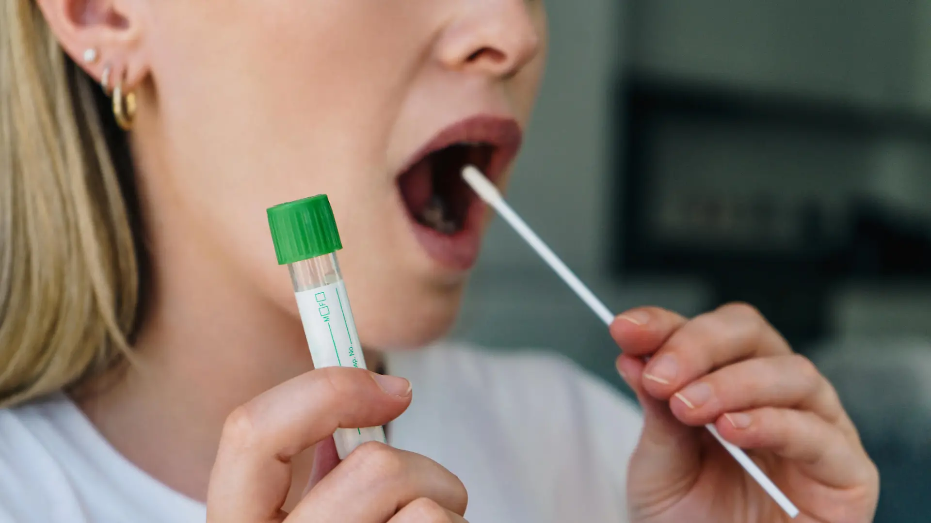 Young woman holds a swab into her mouth and holding a medical tube for the coronavirus / covid19 home test