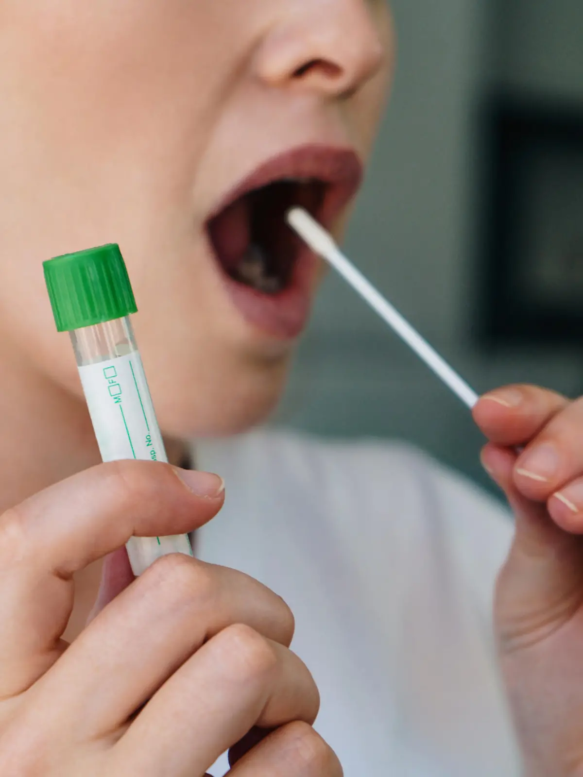 Young woman  holds a swab into her mouth and holding a medical tube for the coronavirus / covid19 home test