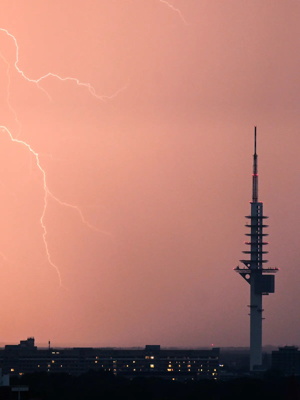 ARCHIV - 09.07.2023, Niedersachsen, Hannover: Ein Blitz entlädt sich während eines Gewitters hinter dem Fernmeldeturm Telemax in Hannover.      (zu dpa «20 Warnungen via Cell Broadcast in Niedersachsen») Foto: Julian Stratenschulte/dpa +++ dpa-Bildfunk +++