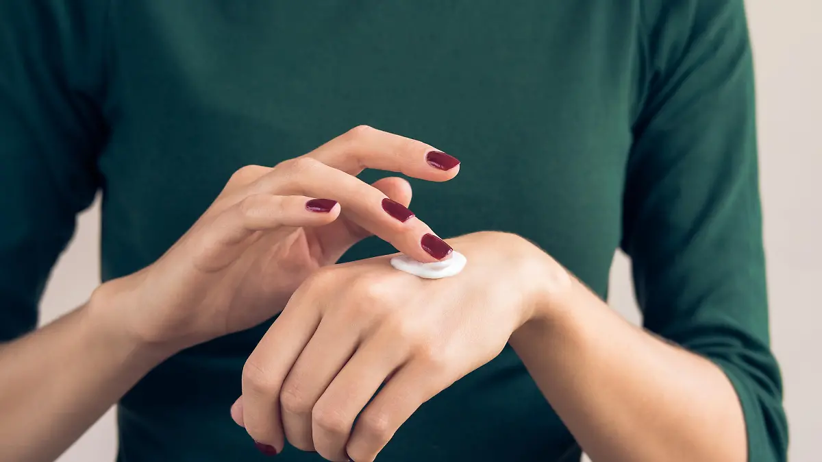 Woman in a green T-shirt and a maroon manicure applying hand cream