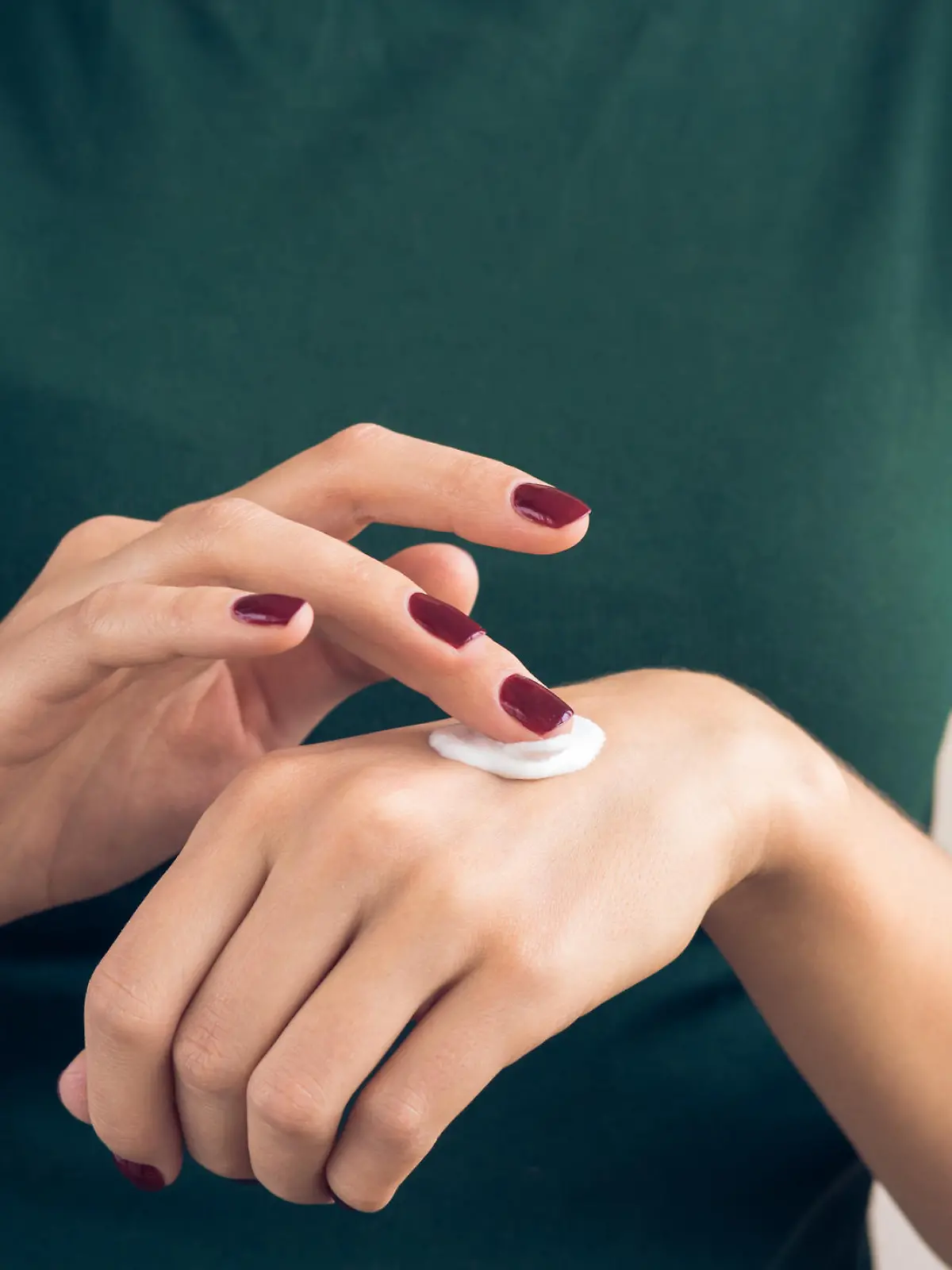 Woman in a green T-shirt and a maroon manicure applying hand cream