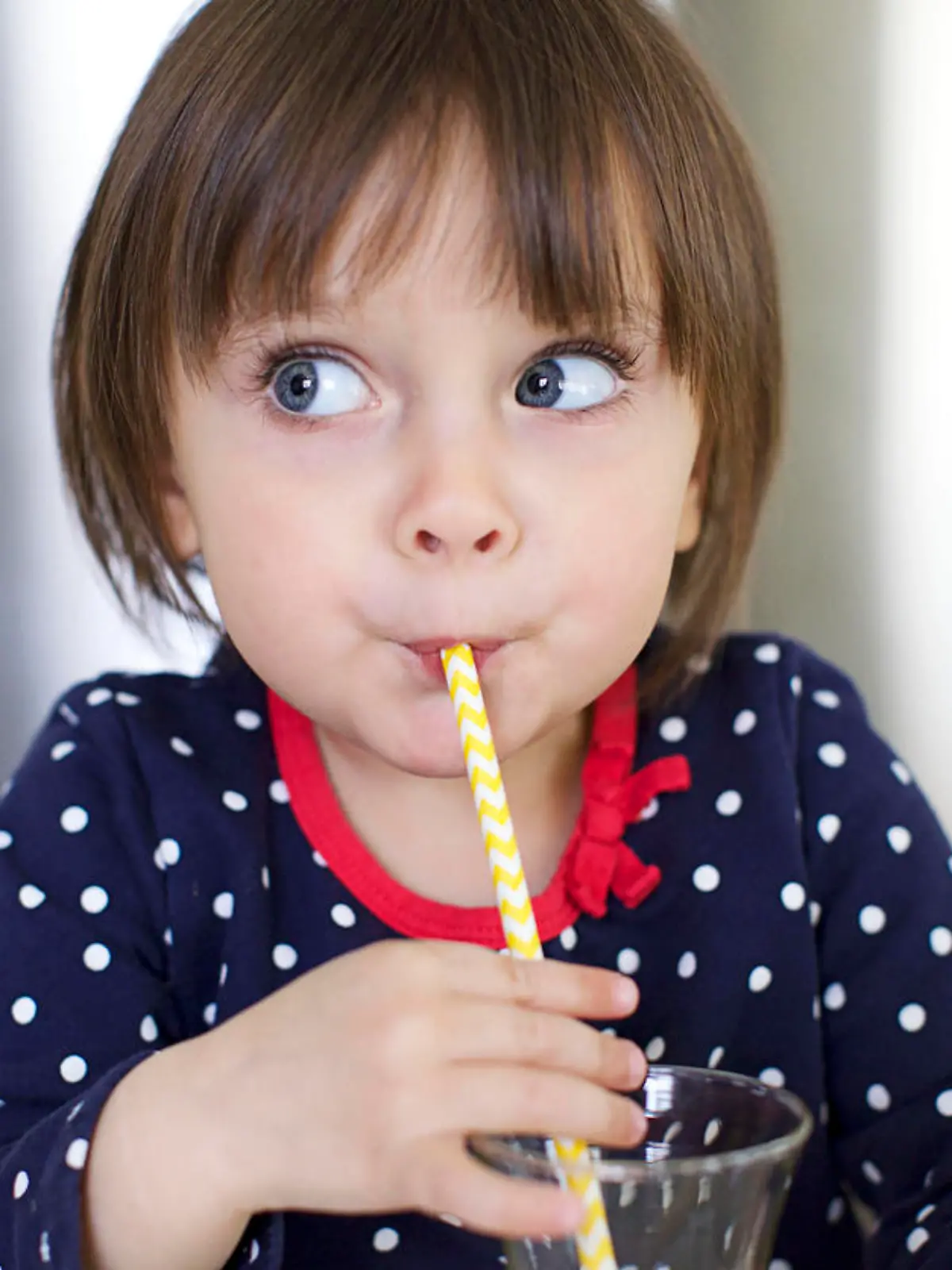 Cute Little Girl is Drinking Water With a Paper Straw and Making Faces