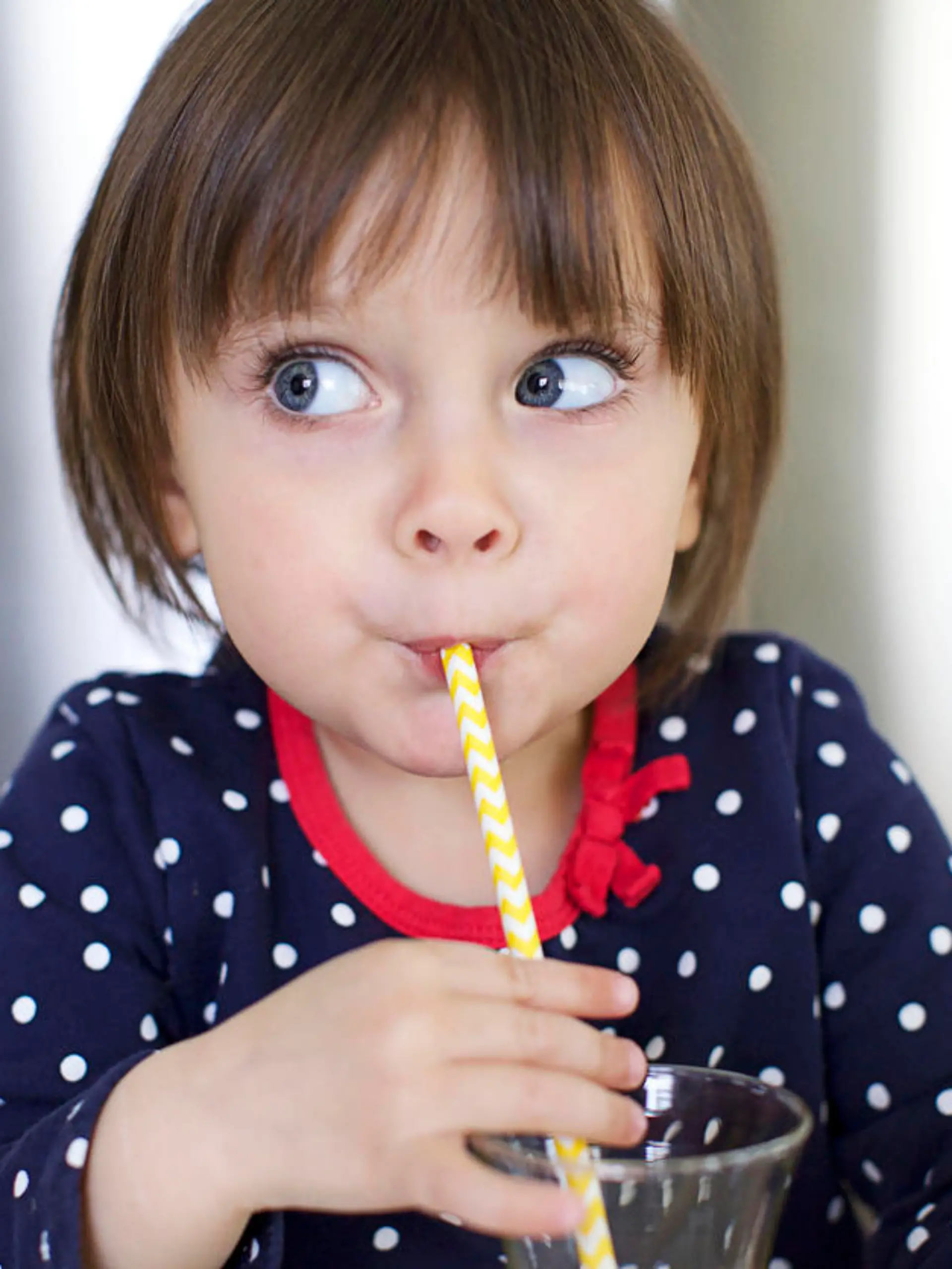 Cute Little Girl is Drinking Water With a Paper Straw and Making Faces