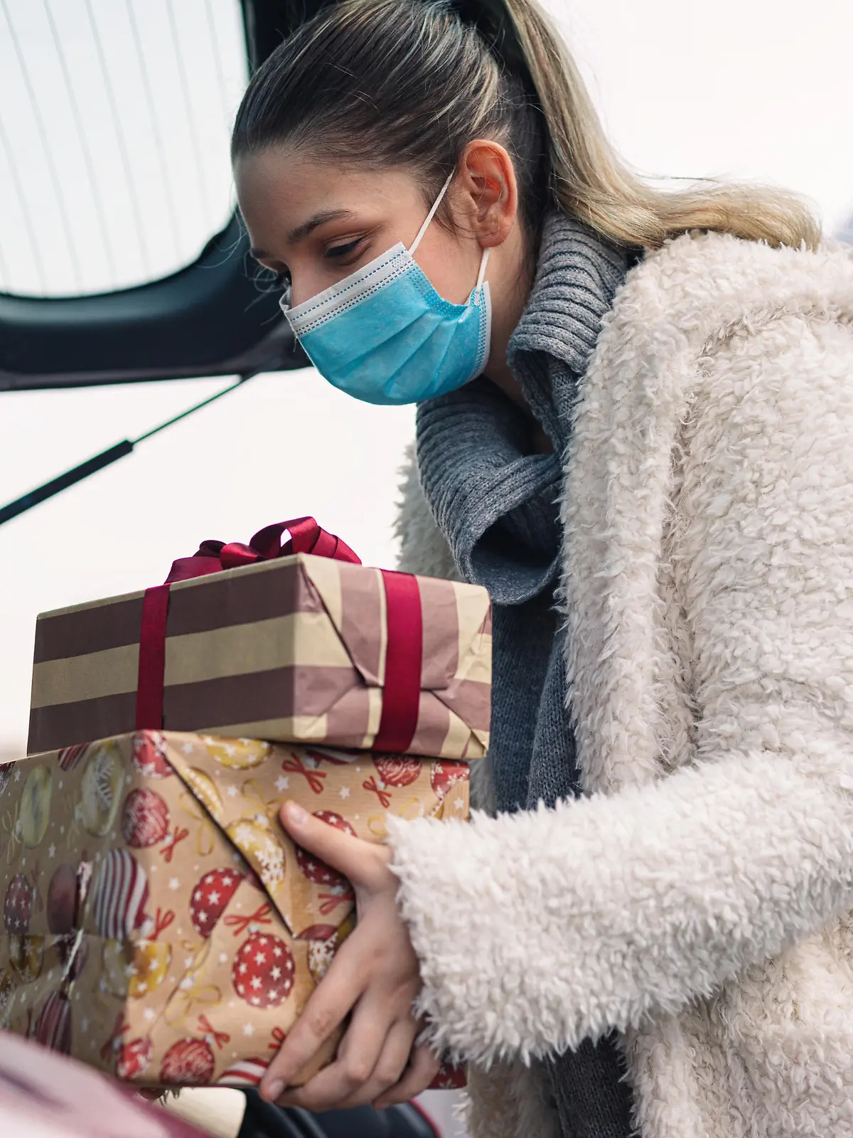 Teenage girl packing Christmas gifts in a car after shopping. She wears a protective mask to protect from corona virus COVID-19.