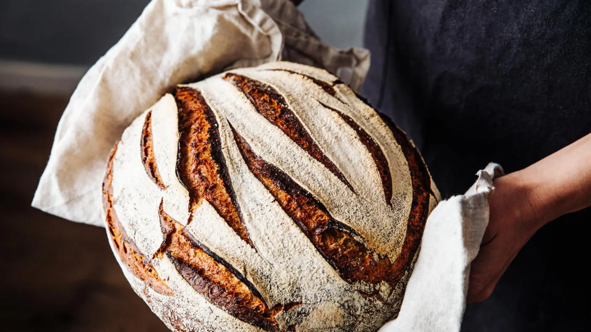 Close-up of fresh baked sourdough bread. Woman is holding wheat and rye beard. She is in kitchen.