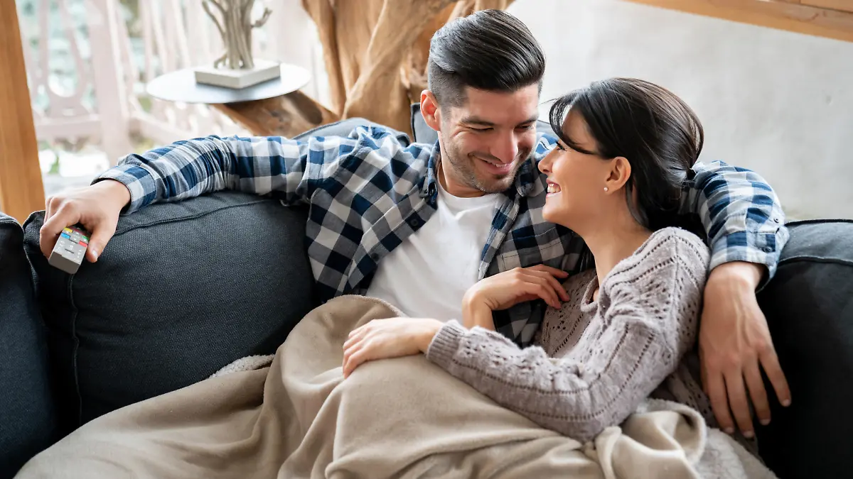 Portrait of a loving couple watching tv in their winter lodge while lying on the sofa looking very happy - lifestyle concepts