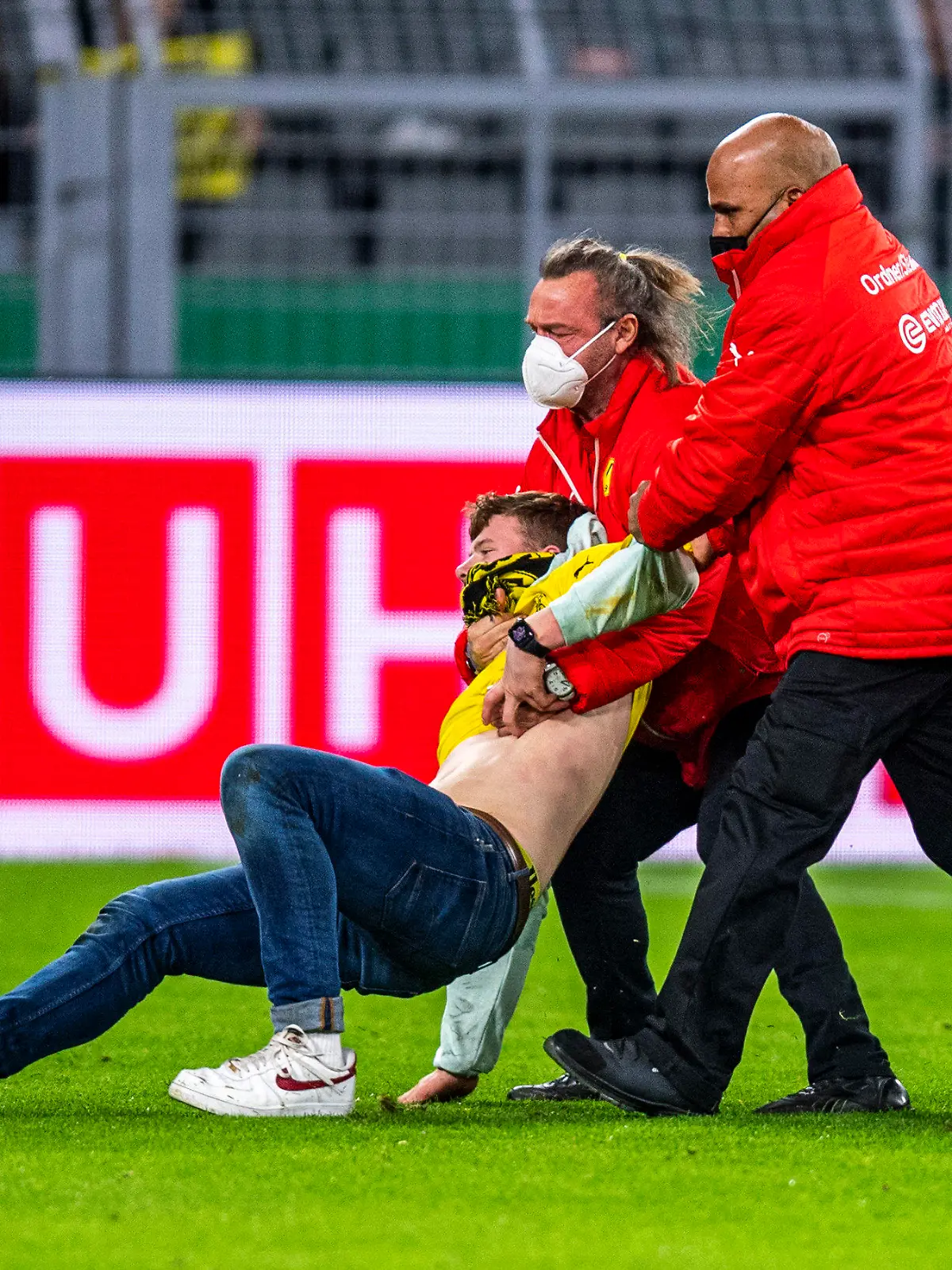 26.10.2021, Nordrhein-Westfalen, Dortmund: Fußball: DFB-Pokal, Borussia Dortmund - FC Ingolstadt 04, 2. Runde, Signal Iduna Park: Ordner bringen einen Fan, der auf das Spielfeld gelaufen ist, vom Feld. Foto: David Inderlied/dpa - WICHTIGER HINWEIS: Gemäß den Vorgaben der DFL Deutsche Fußball Liga bzw. des DFB Deutscher Fußball-Bund ist es untersagt, in dem Stadion und/oder vom Spiel angefertigte Fotoaufnahmen in Form von Sequenzbildern und/oder videoähnlichen Fotostrecken zu verwerten bzw. verwerten zu lassen. +++ dpa-Bildfunk +++