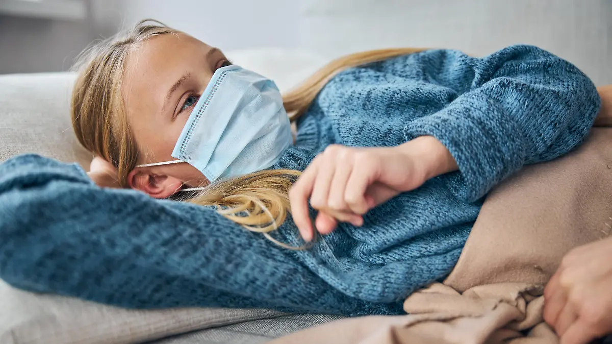 Low-spirited female child in a face mask lying on the sofa at home in broad daylight
