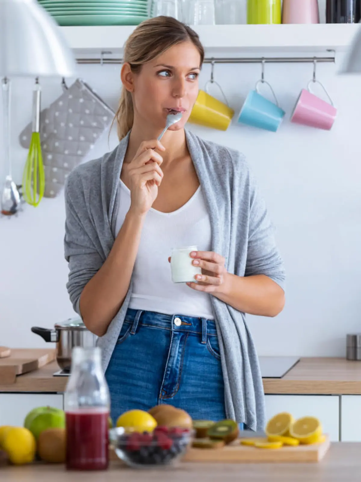Shot of pretty young woman eating yogurt while standing in the kitchen at home.