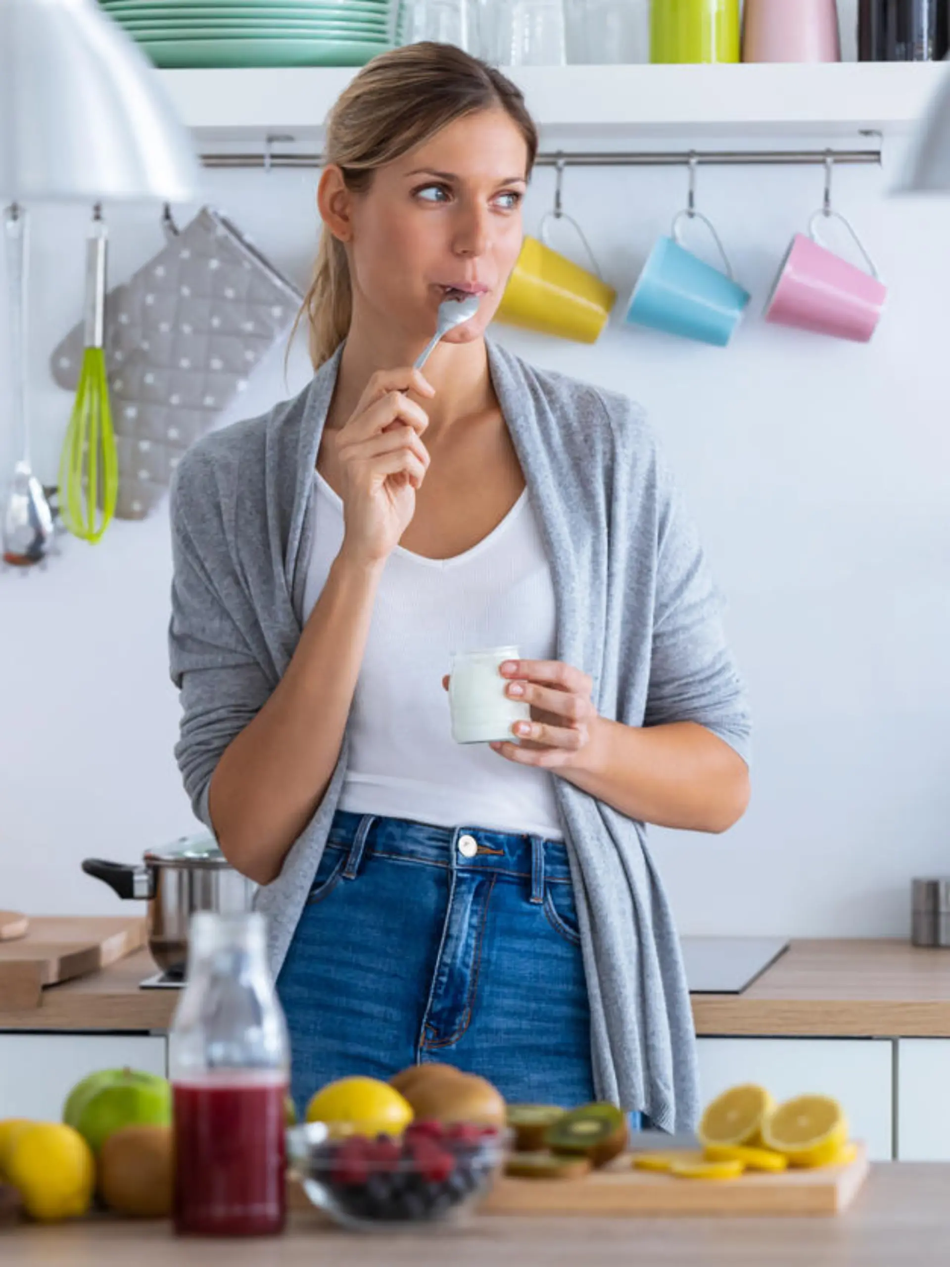 Shot of pretty young woman eating yogurt while standing in the kitchen at home.