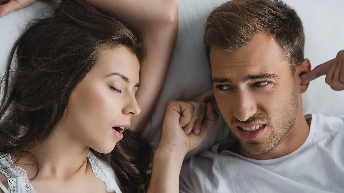 top view of man closing ears and looking at snoring wife in bed