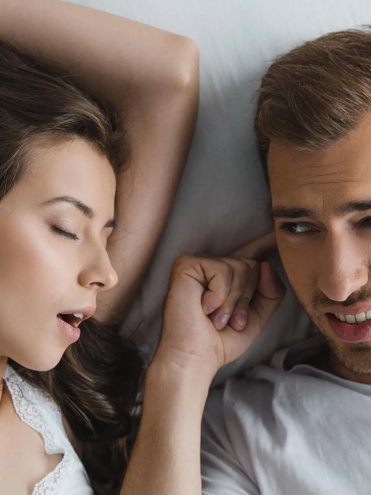 top view of man closing ears and looking at snoring wife in bed