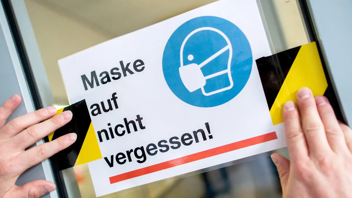 ARCHIV - 25.08.2020, Niedersachsen, Oldenburg: Der Hausmeister des Neuen Gymnasiums in Oldenburg klebt ein Schild mit der Aufschrift «Maske auf nicht vergessen!» an die Glasscheibe einer Zwischentür. (zu dpa: "Widerstand gegen Corona-Maßnahmen bringt Unruhe in Schulen") Foto: Hauke-Christian Dittrich/dpa +++ dpa-Bildfunk +++