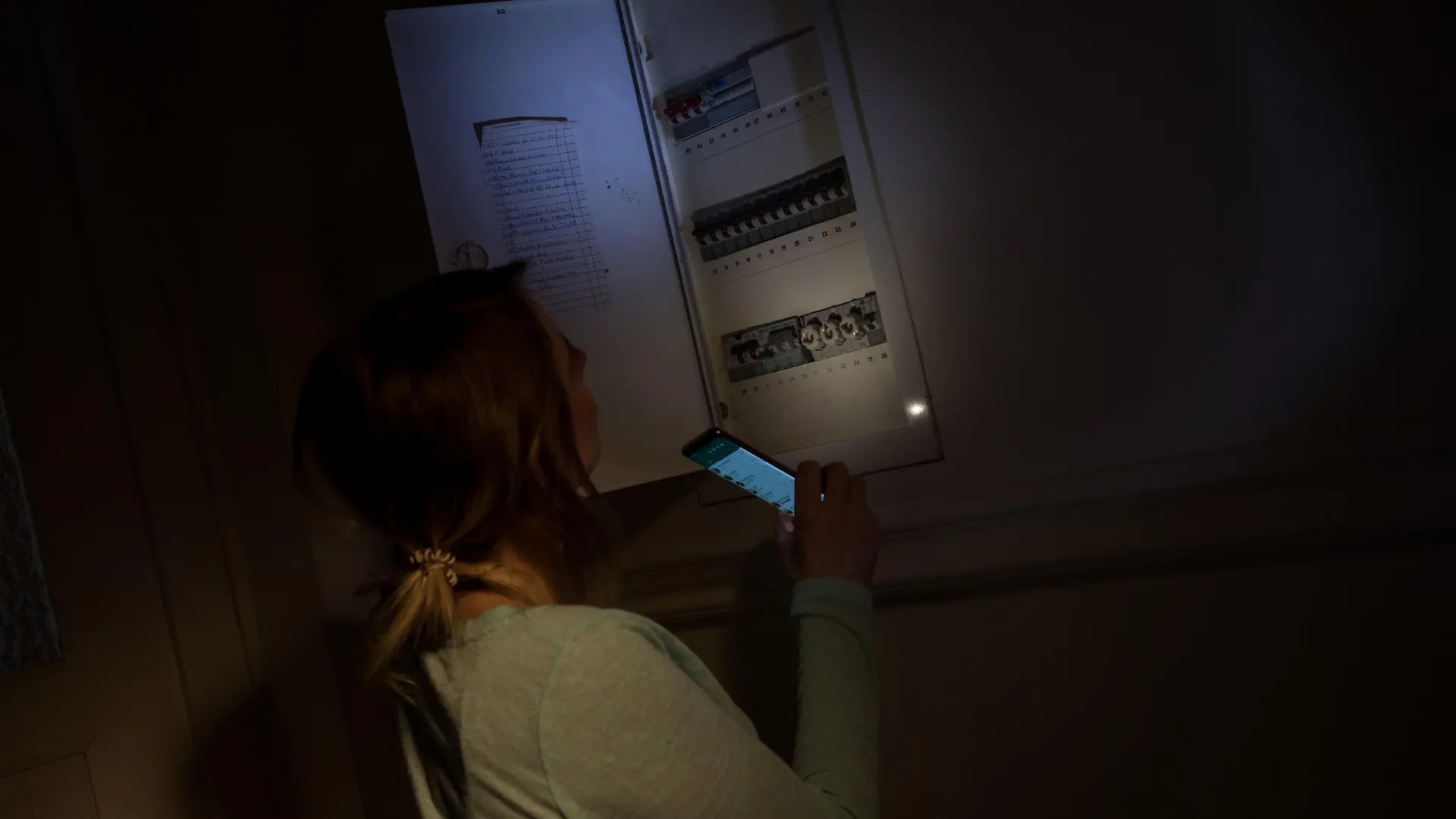 ILLUSTRATION - Eine junge Frau schaut am 29.01.2020 in einer Wohnung in Wittenberge waehrend eines Stromausfalls mit Hilfe der Taschenlampe auf ihrem Smartphone in den Sicherungskasten (gestellte Szene). Foto: Christin Klose