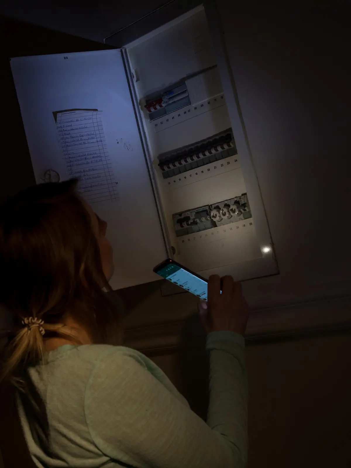 ILLUSTRATION - Eine junge Frau schaut am 29.01.2020 in einer Wohnung in Wittenberge waehrend eines Stromausfalls mit Hilfe der Taschenlampe auf ihrem Smartphone in den Sicherungskasten (gestellte Szene). Foto: Christin Klose
