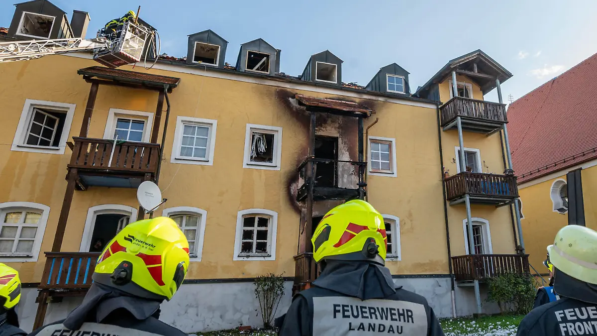 23.10.2021, Bayern, Reisbach: Feuerwehrmänner stehen vor einem ausgebrannten Mehrfamilienhaus. Drei Frauen und ein frühgeborenes Baby sind in dem Haus bei einem Brand ums Leben gekommen. Foto: Armin Weigel/dpa +++ dpa-Bildfunk +++