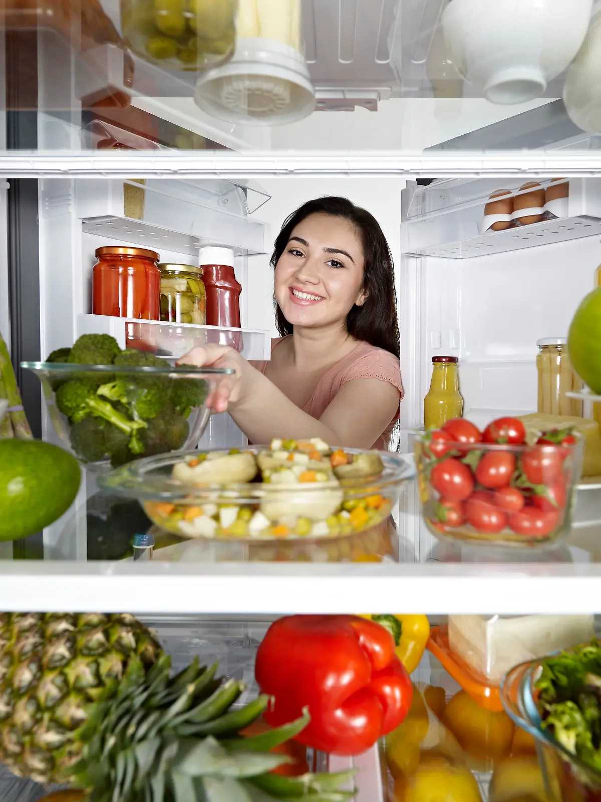 Woman looking at camera out of the fridge.