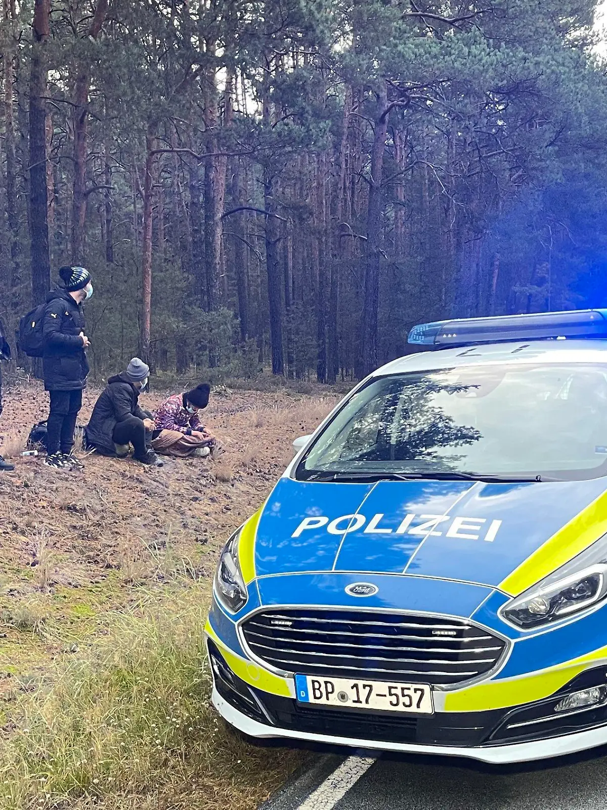 19.10.2021, Brandenburg, Podrosche: Bundespolizisten stehen neben einer Gruppe von Migranten, die zuvor über die deutsch-polnische Grenze gegangen waren. (zu dpa «Zuwanderung via Belarus: Seehofer schreibt an Polens Innenminister») Foto: Danilo Dittrich/dpa-Zentralbild/dpa +++ dpa-Bildfunk +++
