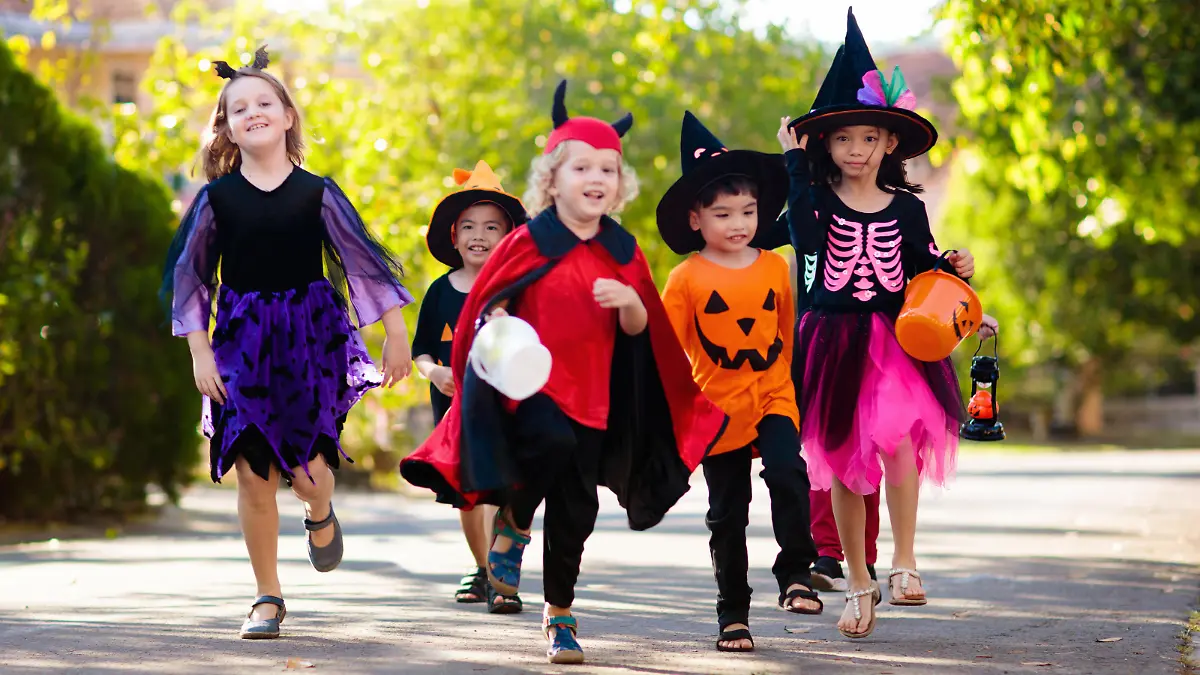 Child in Halloween costume. Mixed race Asian and Caucasian kids trick or treat on suburban street. Little boy and girl with pumpkin lantern and candy bucket. Baby in witch hat. Autumn holiday fun.
