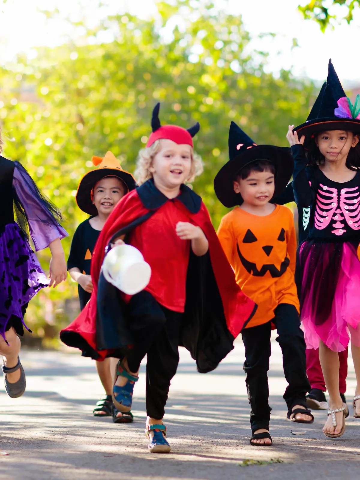 Child in Halloween costume. Mixed race Asian and Caucasian kids trick or treat on suburban street. Little boy and girl with pumpkin lantern and candy bucket. Baby in witch hat. Autumn holiday fun.