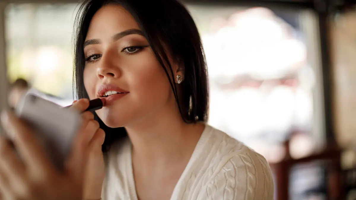 Young woman applying lipstick at a cafe