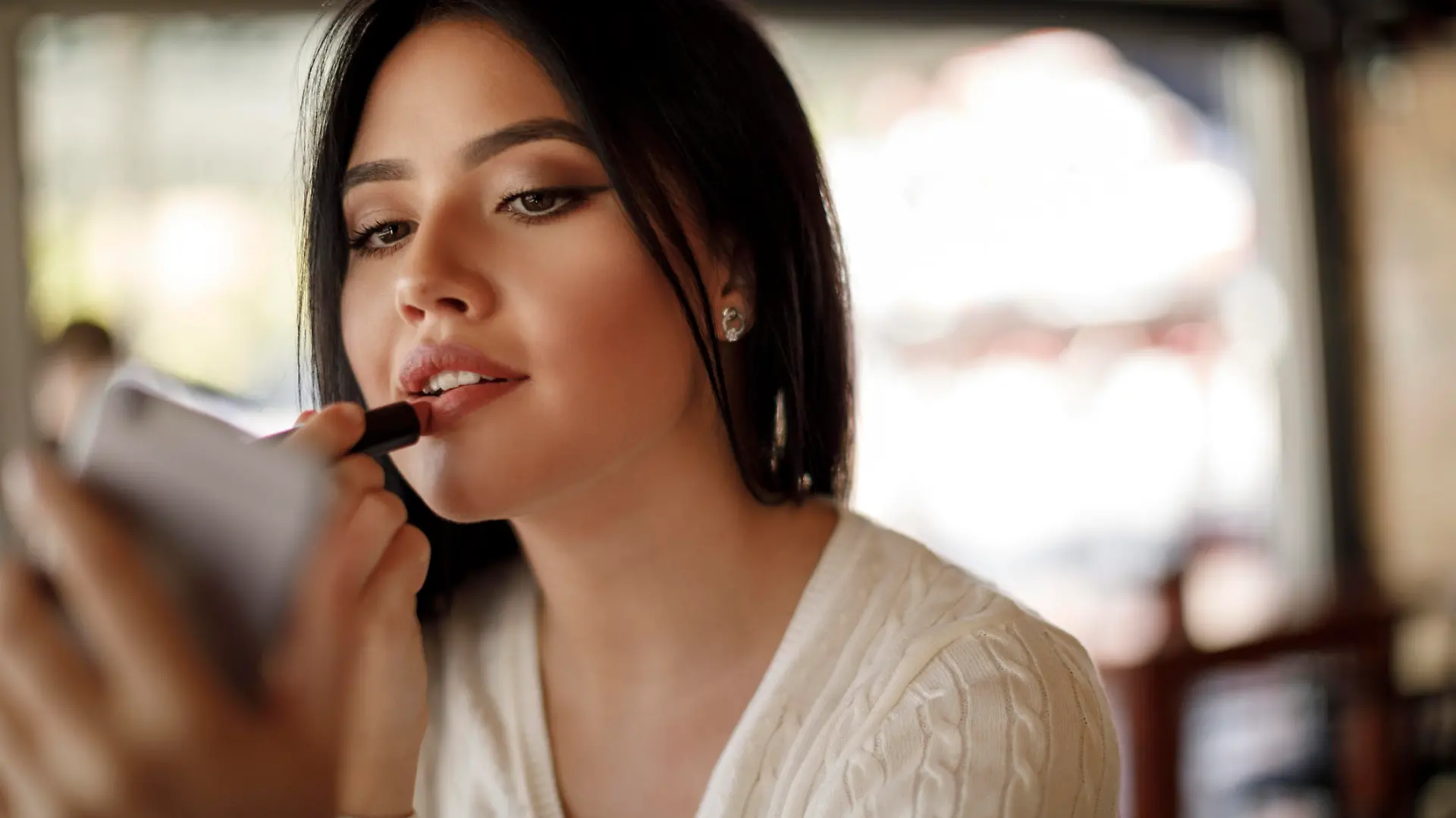 Young woman applying lipstick at a cafe