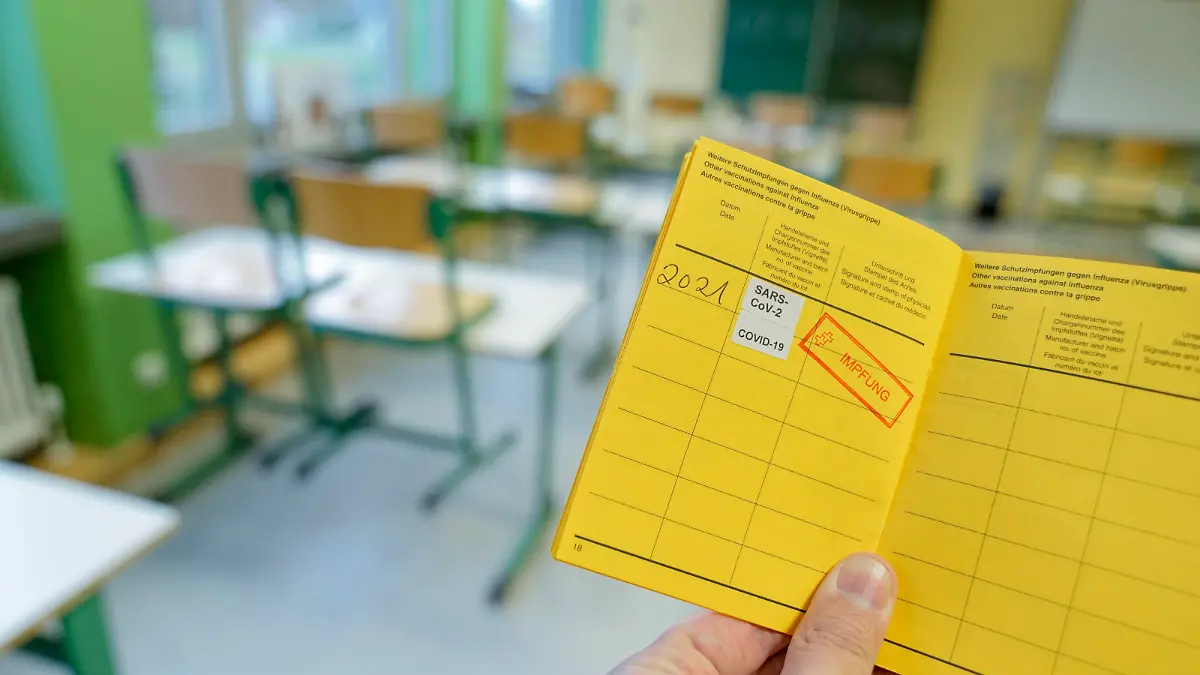 Symbolbild Schule und Klassenzimmer im Lockdown Symbolfoto eines Impfpass mit Impfstempel gegen das Coronavirus mit Klassenzimmer einer Schule im Hintergrund. Wann werden Lehrer und Schueler geimpft. Deutschland *** Symbolic image school and classroom in lockdown Symbolic photo of a vaccination certificate with vaccination stamp against the coronavirus with classroom of a school in the background When will teachers and students be vaccinated Germany